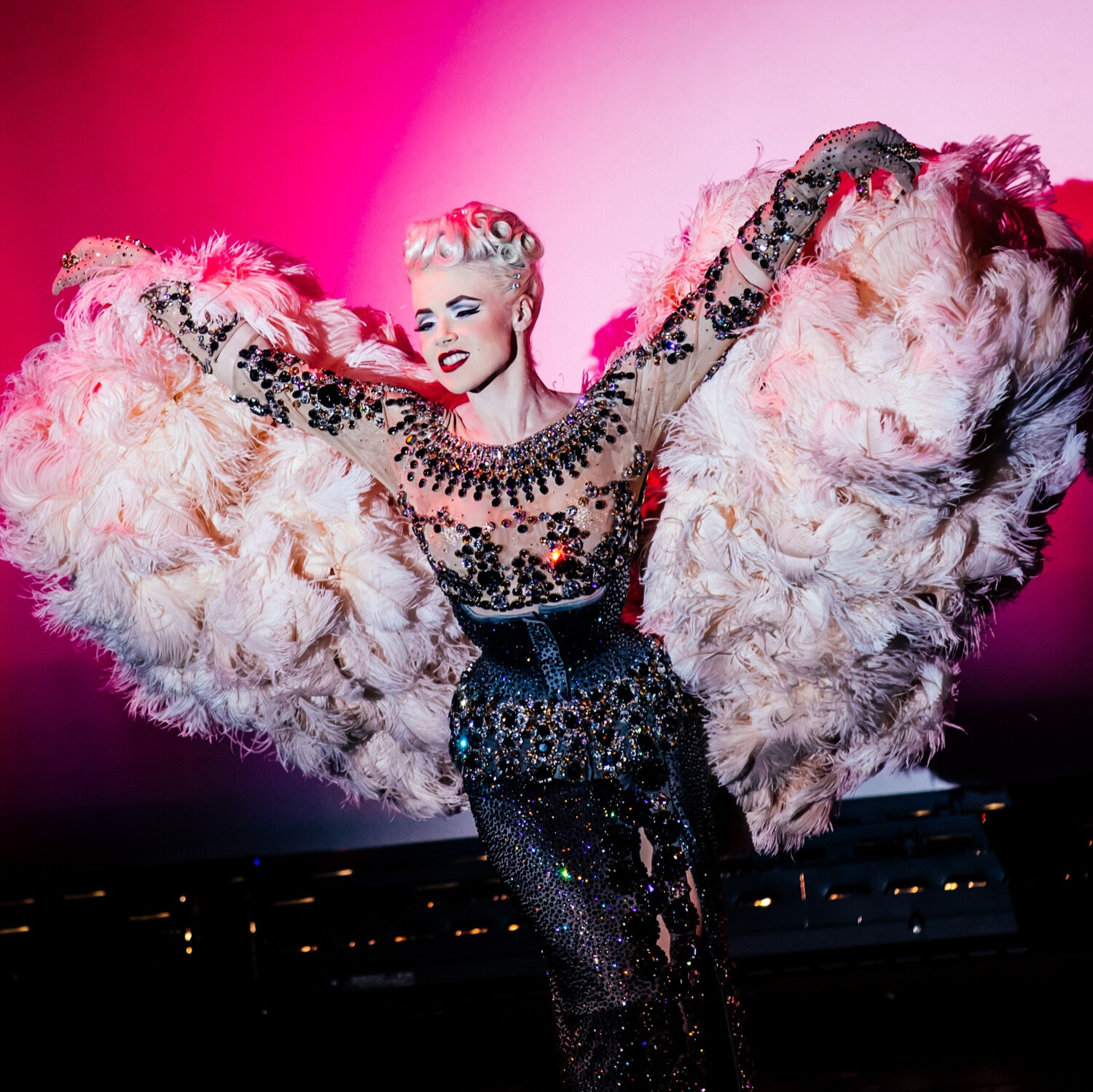 Internationally known burlesque artist and model, Mosh, from Los Angeles performing with Adèle Wolf Productions in Oklahoma City. She wears a decadently embellished dark gray and nude costume covered in rhinestones with a giant, ostrich plume, cream colored boa.